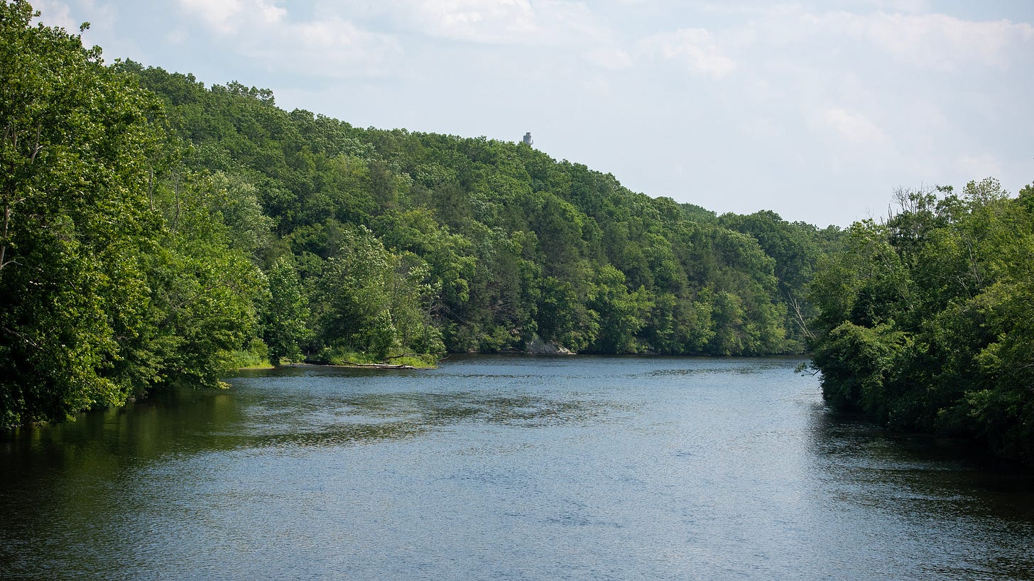 The river moves quietly between wooded banks where industry once stood