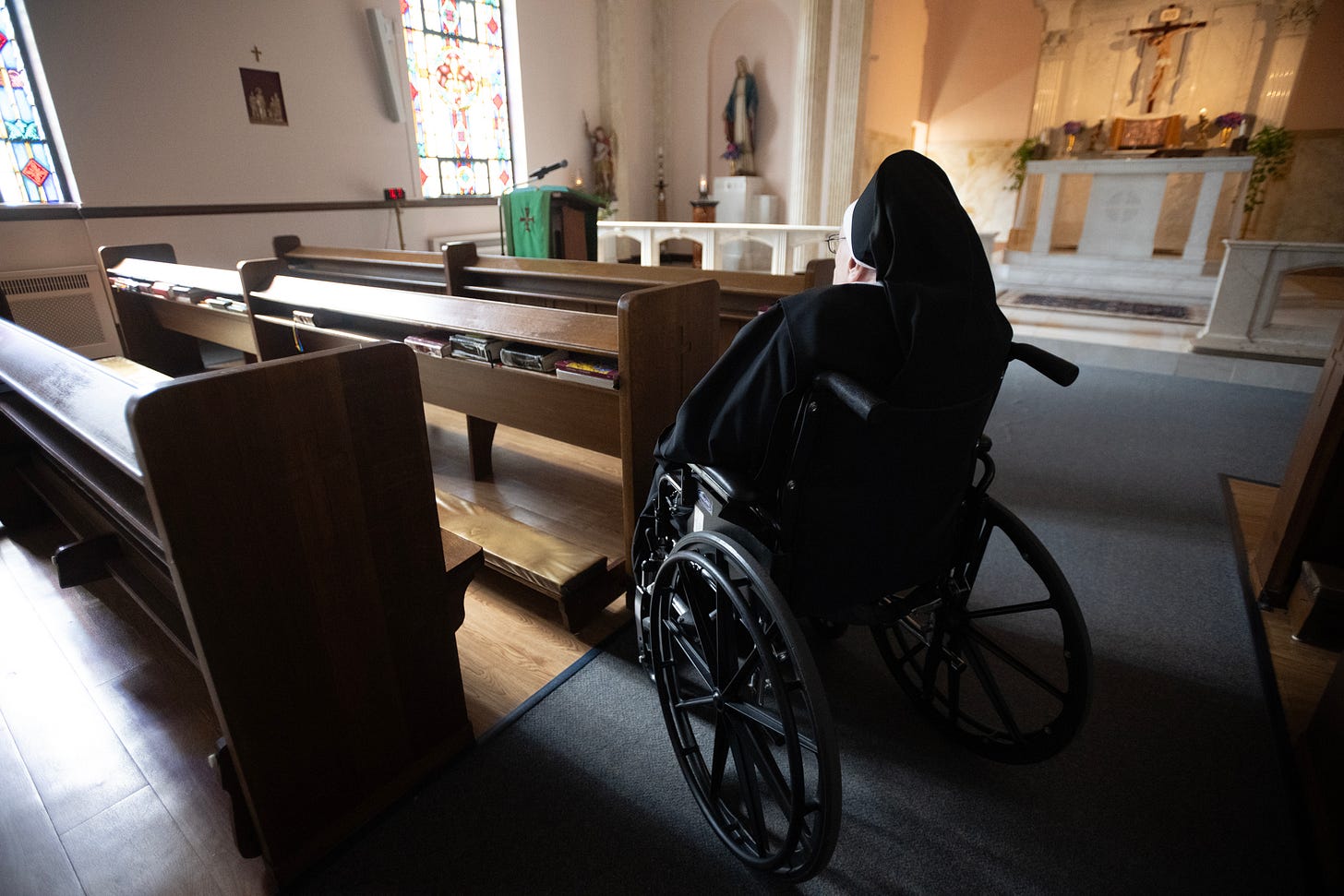 An elderly Sister prays from her wheelchair before the altar