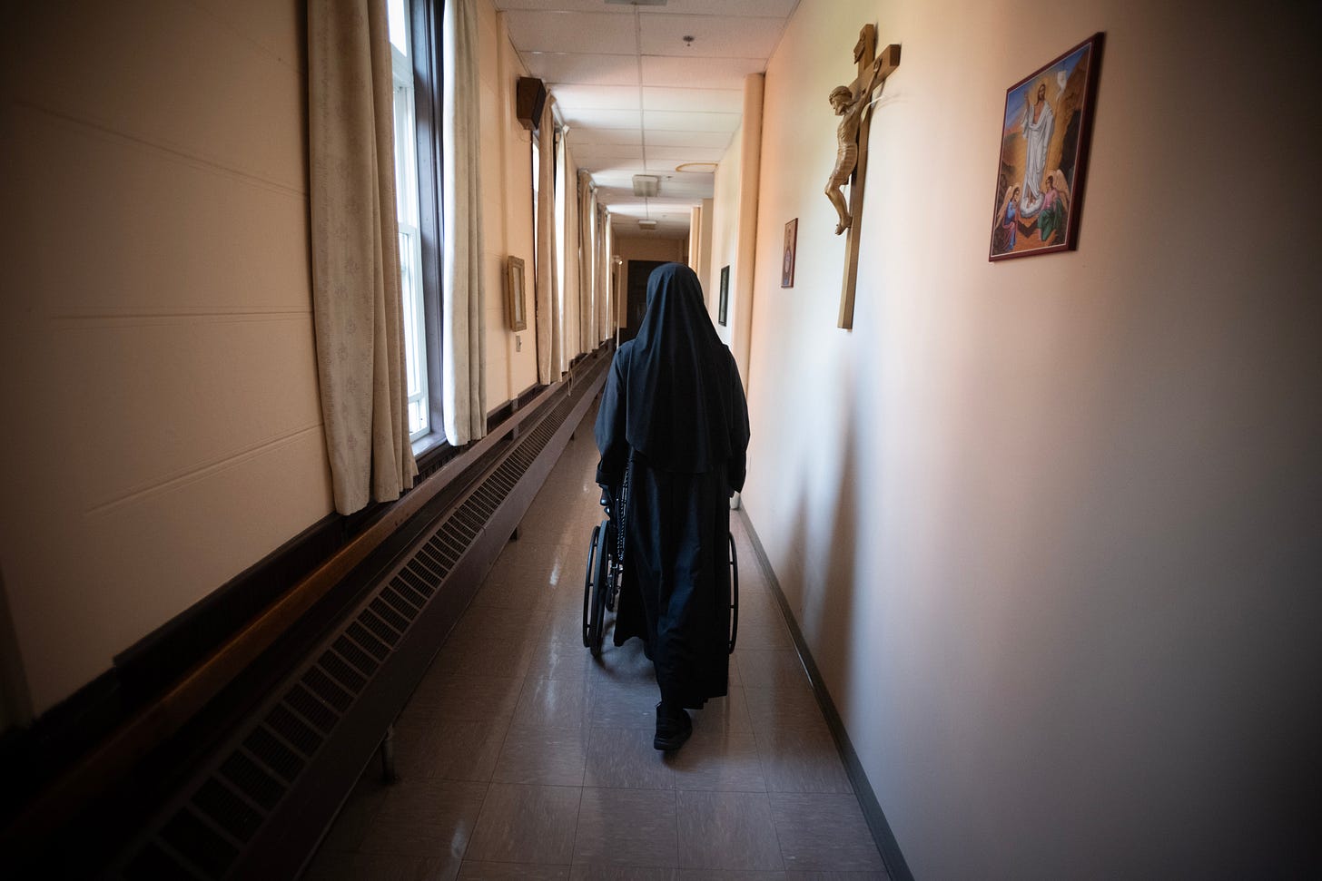 A Sister pushes an elderly member of the community down a long corridor