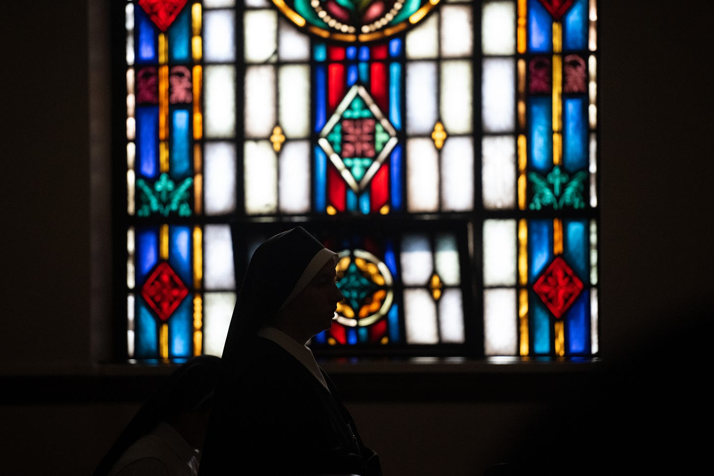 A Sister stands in silhouette before a stained-glass window
