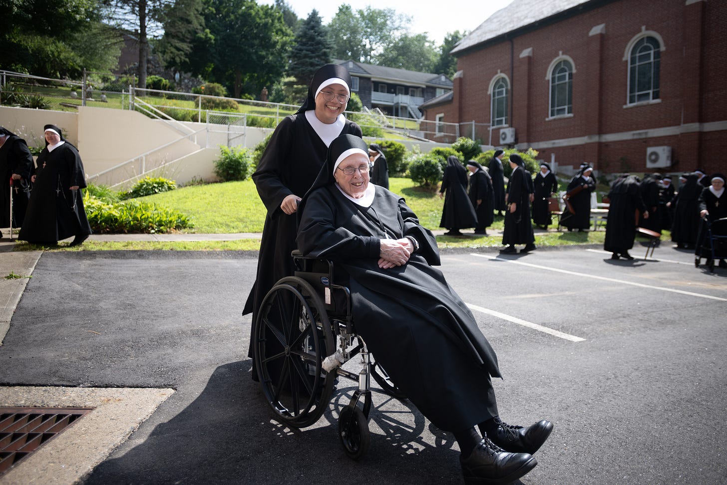 A Sister in a wheelchair smiles as the community gathers behind her