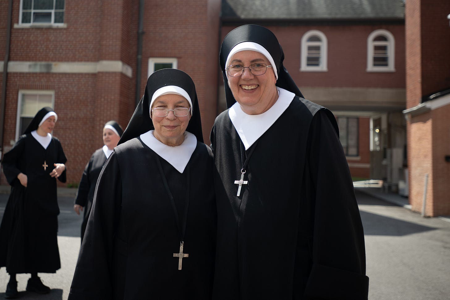 Two Sisters stand together as the larger community gathers in the courtyard